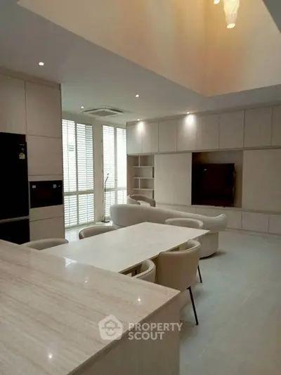 Spacious modern living room with open kitchen and elegant dining area, featuring sleek furniture and ample natural light.