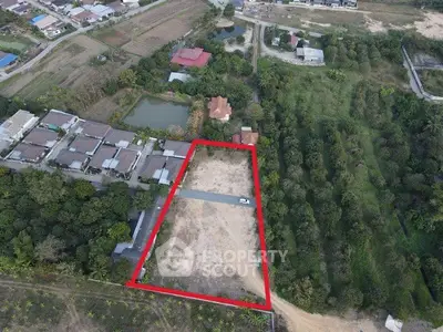 Aerial view of a large plot of land outlined in red, surrounded by greenery and residential buildings.