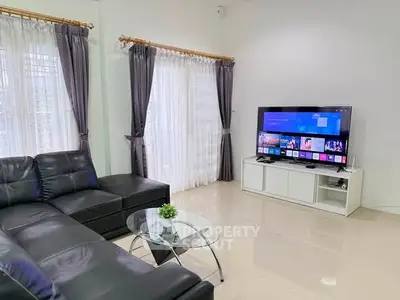 Modern living room with sleek black leather sofa and large TV, perfect for entertainment.