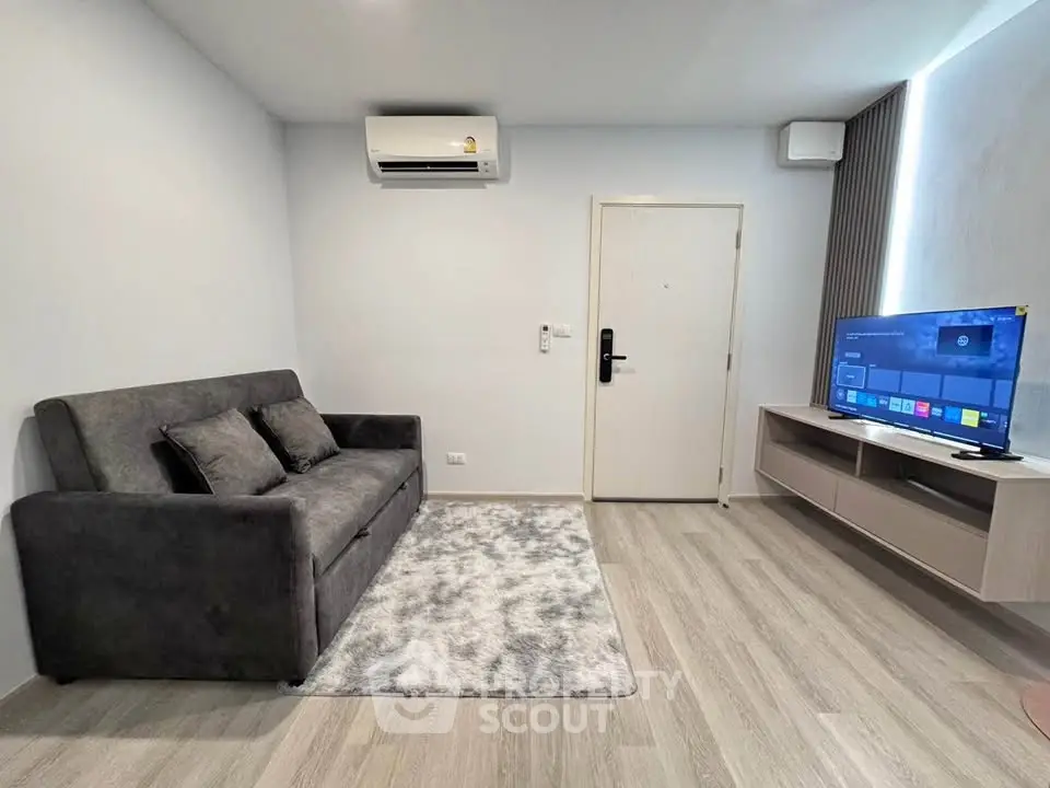 Modern living room with sleek sofa, wall-mounted TV, and air conditioning in a stylish apartment.