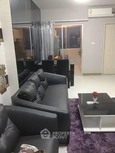 Modern living room with sleek black sofa and glass dining table, featuring a cozy ambiance.