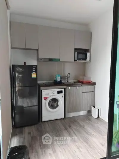 Compact modern kitchen with washing machine and microwave, ideal for urban living.