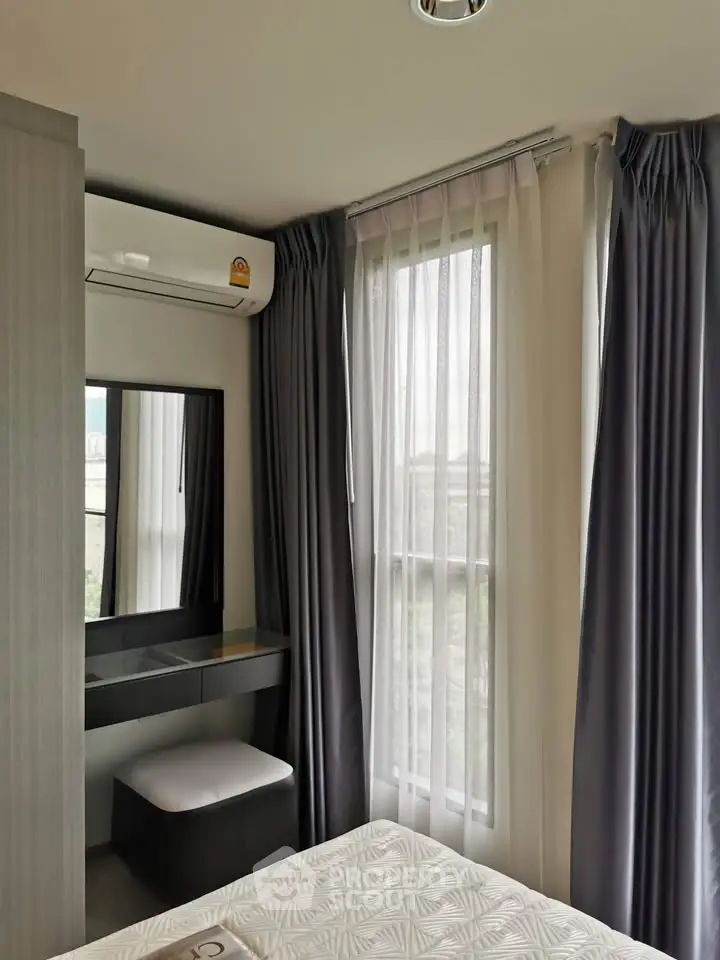 Cozy bedroom with modern decor and natural light from large windows, featuring a stylish vanity area.