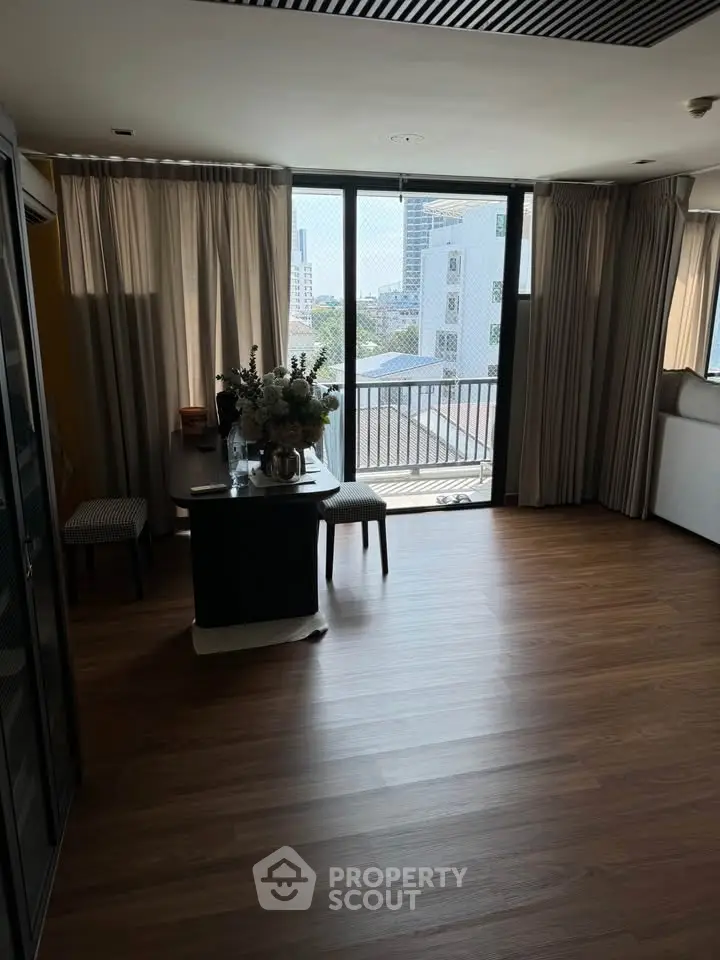 Spacious living room with large windows and city view, featuring elegant decor and wooden flooring.