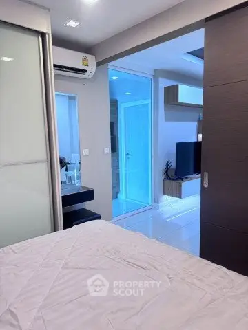 Modern bedroom with sliding door and view into living area, featuring sleek design and ambient lighting.