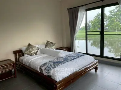 Spacious bedroom with large window offering serene water view, featuring elegant decor and natural light.