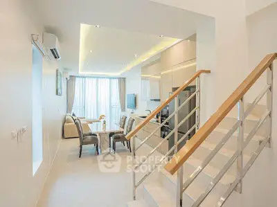 Modern open-plan living room with dining area and staircase, featuring sleek design and ample natural light.
