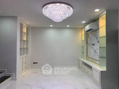 Luxurious living room with elegant chandelier and marble flooring, featuring built-in shelves and air conditioning.