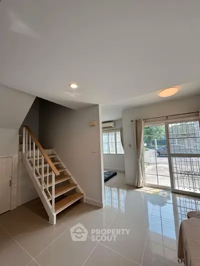 Modern living room with staircase and large windows in a bright, open space.