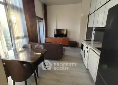 Modern living room with open kitchen and washing machine, featuring sleek furniture and large windows.