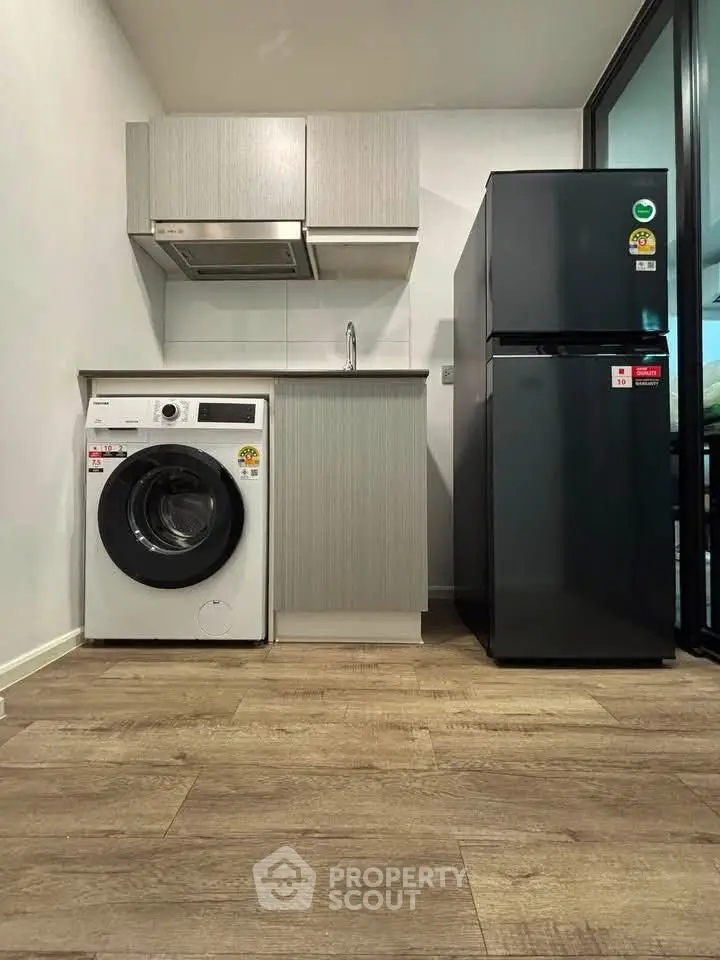 Modern compact kitchen with washing machine and fridge in sleek apartment.
