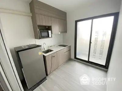 Modern compact kitchen with sleek cabinetry and large sliding glass door.