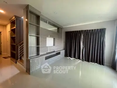 Spacious modern living room with sleek built-in shelving and large window draped with curtains.