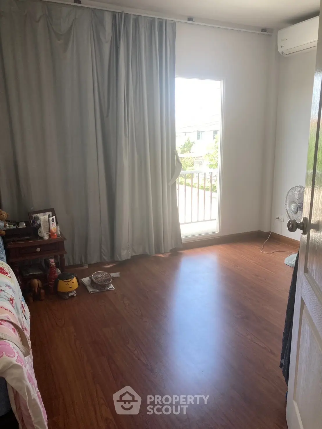 Cozy bedroom with wooden flooring and natural light from balcony window.