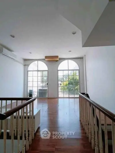 Spacious living area with large arched windows and wooden flooring, offering abundant natural light.