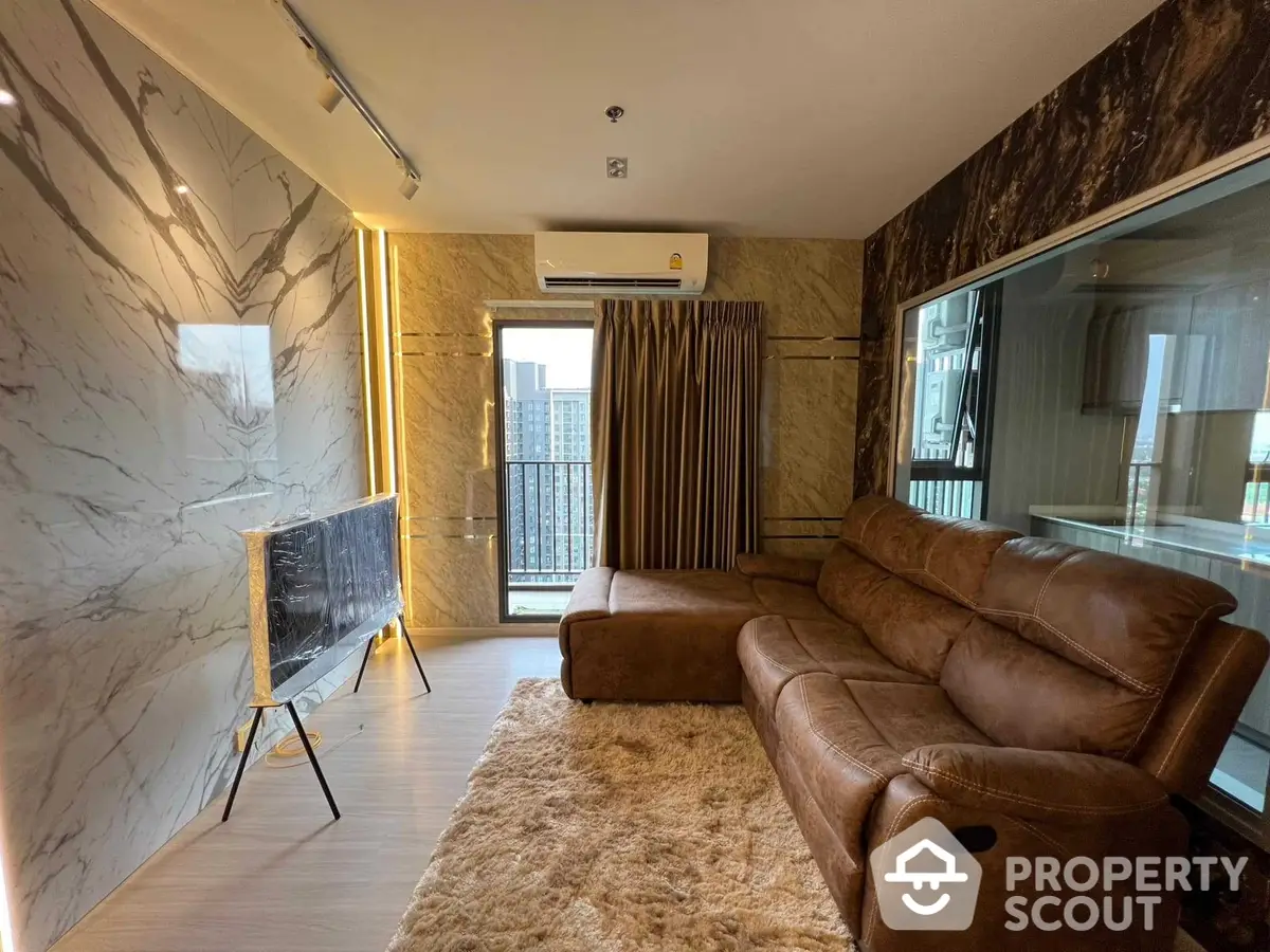 Luxurious living room with marble walls, plush leather sofas, and modern amenities, leading to a sunlit balcony with a view.