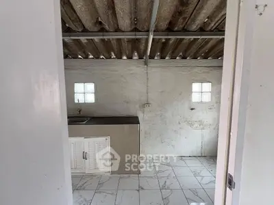 Rustic kitchen with corrugated metal roof and minimalist design, featuring a small window and tiled floor.