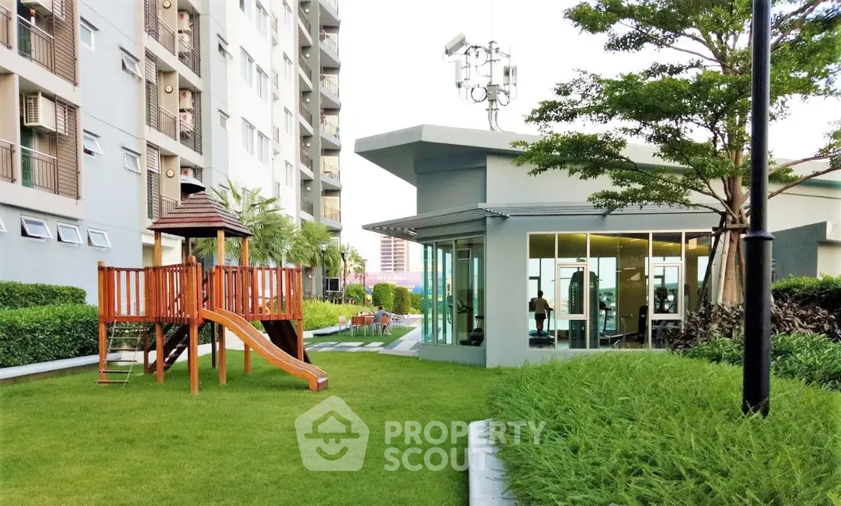 Modern apartment complex with lush garden and children's play area, featuring a sleek glass-walled gym.