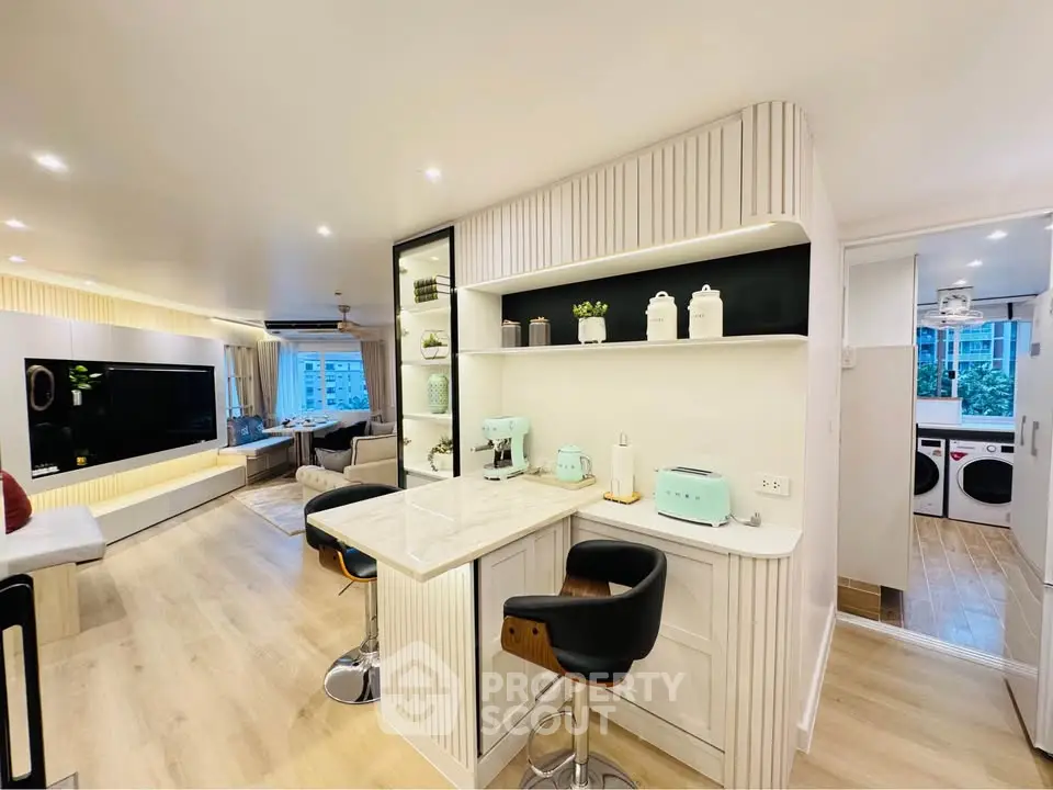 Modern open-plan living room with stylish kitchen and bar seating, featuring sleek appliances and elegant decor.