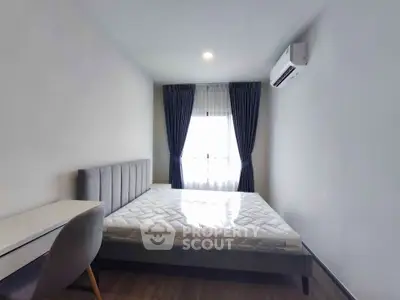 Modern bedroom with natural light, featuring a bed, desk, and air conditioning.