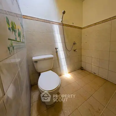 Spacious bathroom with tiled walls and floor, featuring a toilet and shower area.