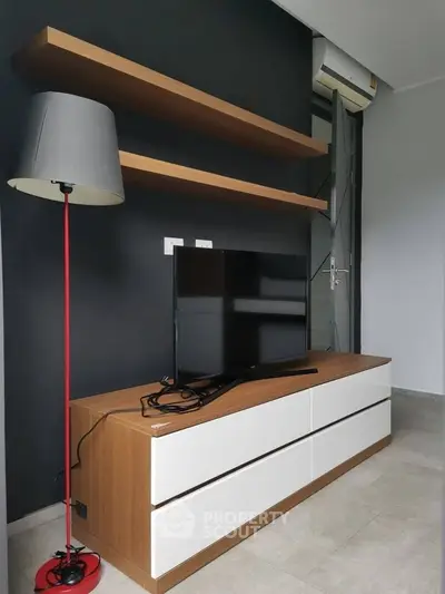 Modern living room with sleek TV stand and floating shelves, featuring stylish floor lamp and air conditioning unit.