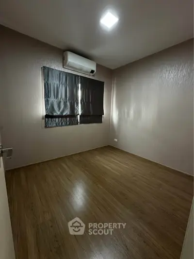 Spacious empty room with wooden flooring and air conditioning, perfect for customization.
