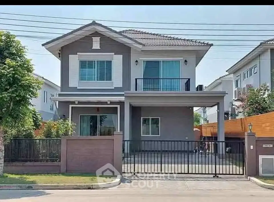 Modern two-story house with gated driveway and balcony in suburban neighborhood.