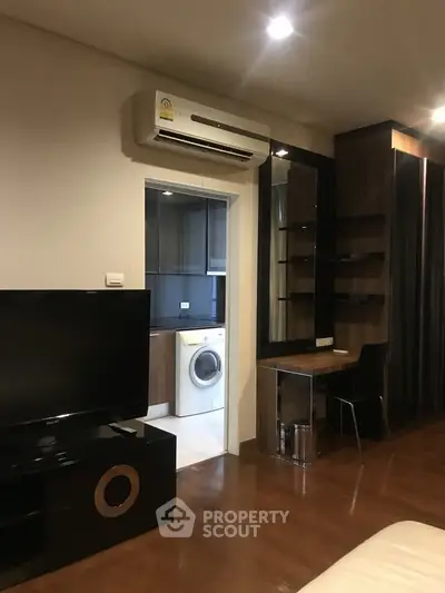 Modern living room with sleek furniture and open view into a compact kitchen with washing machine.