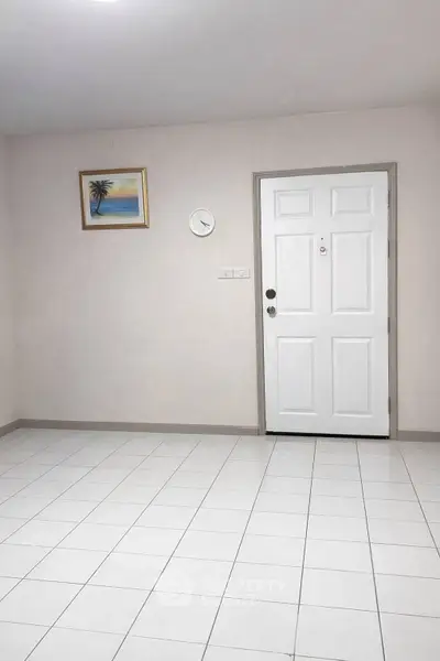 Minimalist interior with white tiled floor and door, featuring a wall clock and framed artwork.