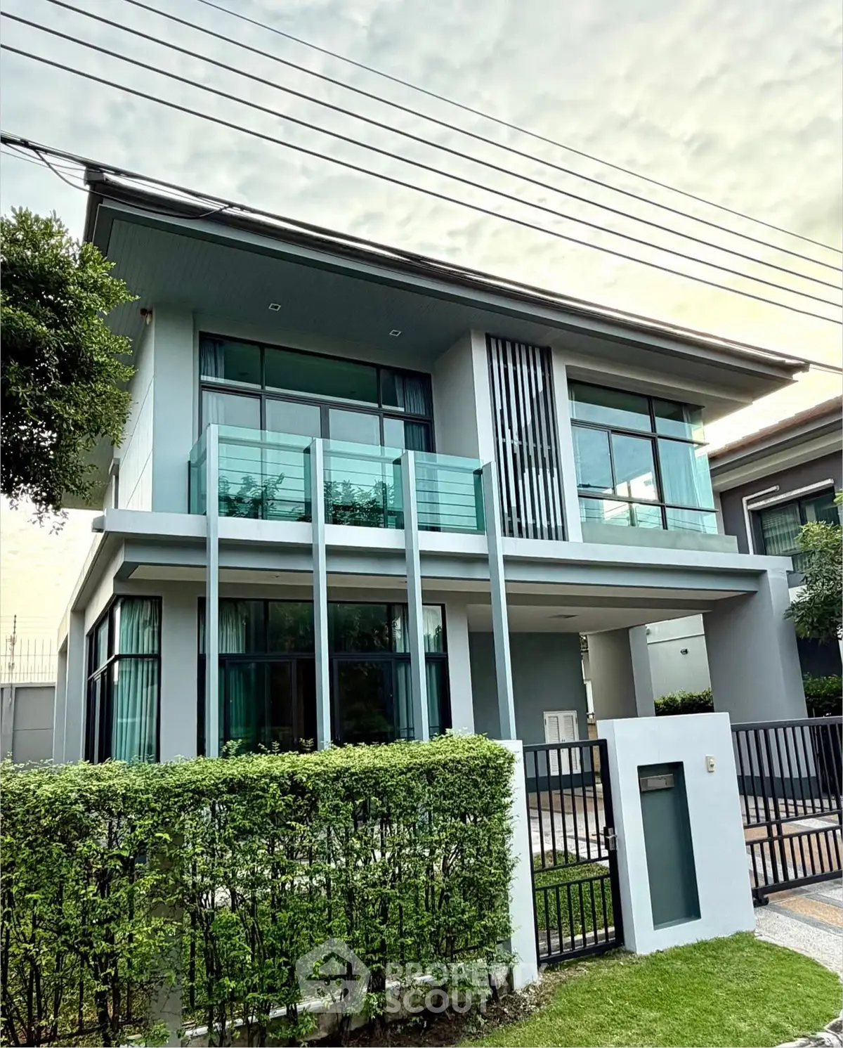 Modern two-story house with glass balcony and lush greenery