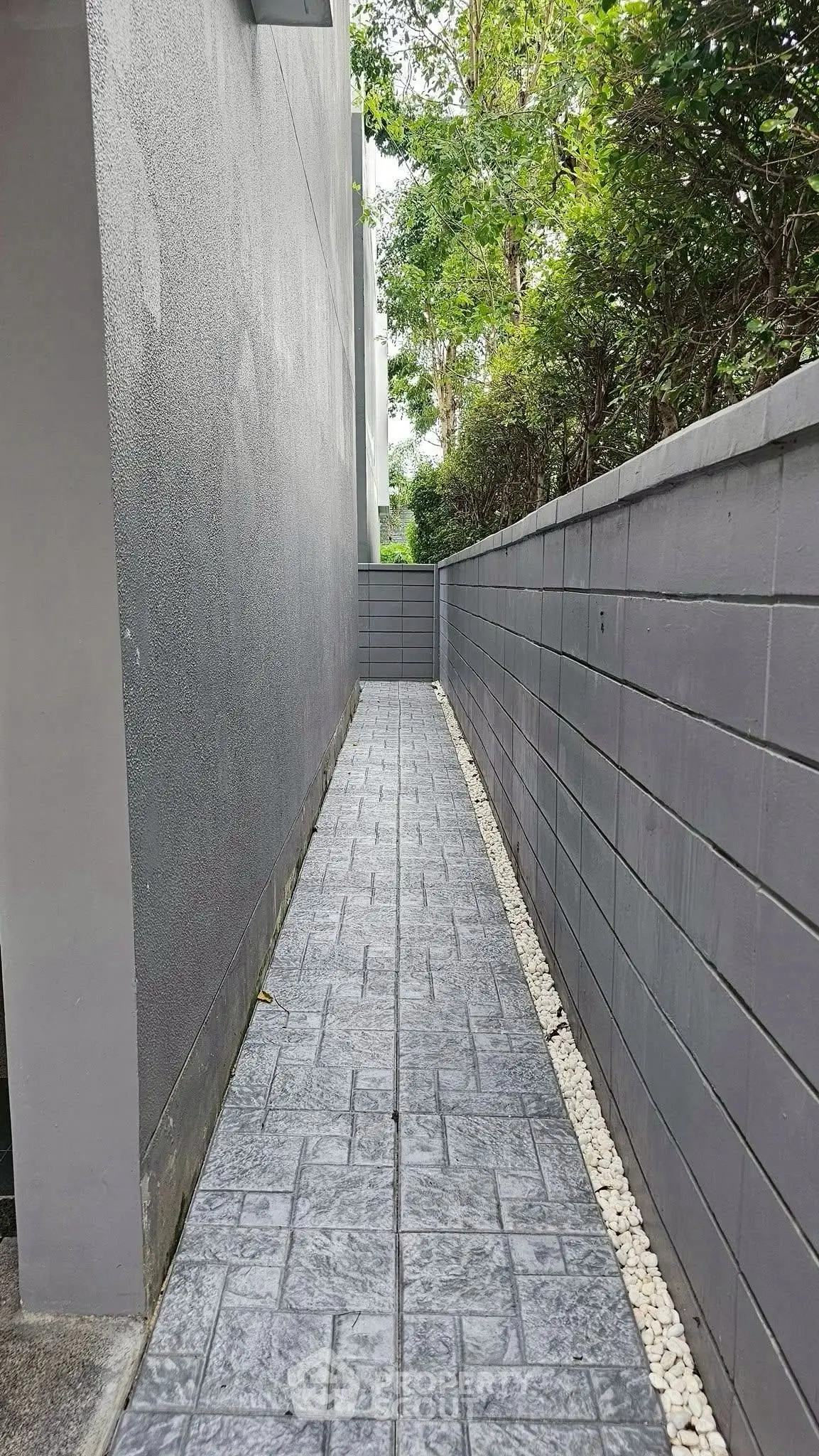 Narrow outdoor pathway with modern gray walls and stone flooring, perfect for minimalist landscaping.