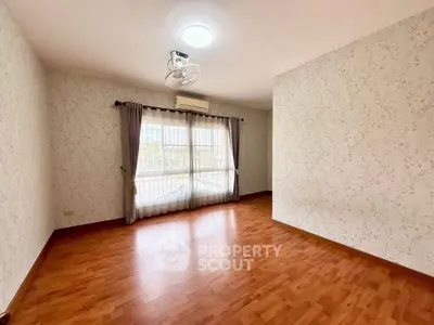 Spacious empty room with wooden flooring and large window, perfect for customization.