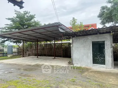 Spacious outdoor parking area with covered carport and adjacent storage room.