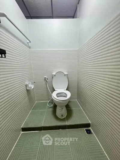 Compact bathroom with elevated toilet and green tiled flooring