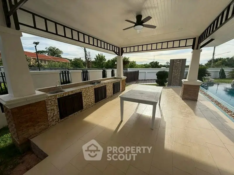 Spacious outdoor patio with poolside view and built-in kitchen area.