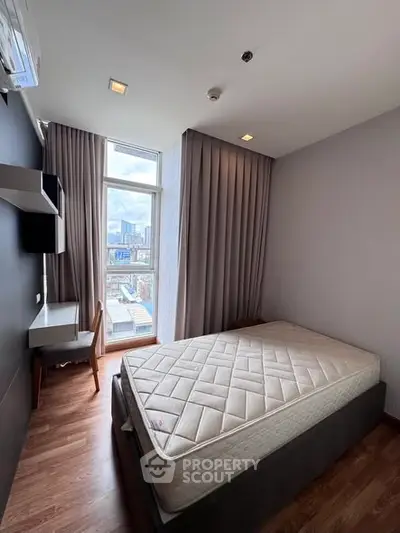 Modern bedroom with city view, featuring a cozy bed and study desk, ideal for urban living.
