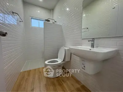 Modern bathroom with white subway tiles and wooden floor, featuring a sleek sink and toilet.