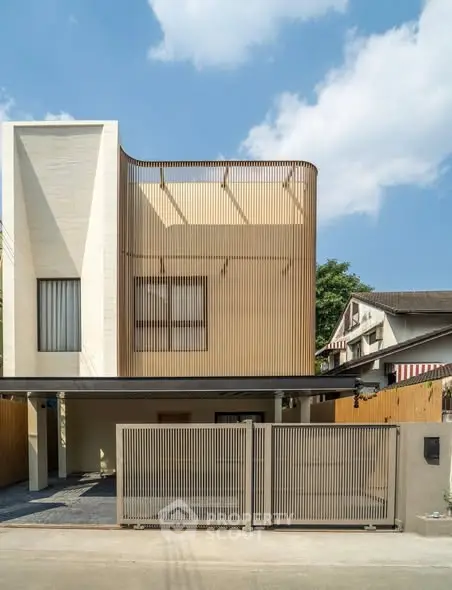 Modern two-story house with sleek facade and gated entrance under clear blue sky.