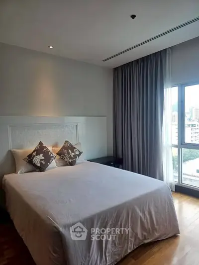 Spacious bedroom with large window and elegant decor in modern apartment.