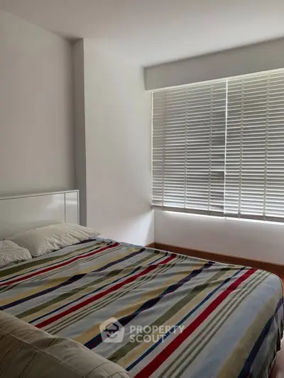 Cozy bedroom with striped bedding and natural light through blinds.
