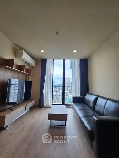 Modern living room with large window and city view, featuring sleek furniture and wooden flooring.