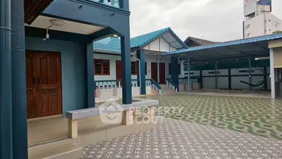 Charming blue-roofed house with spacious tiled courtyard and inviting entrance.