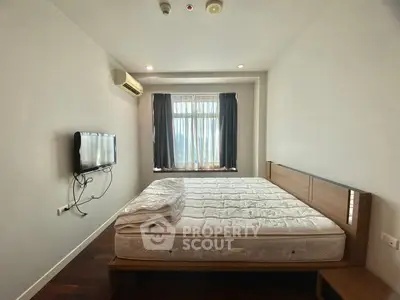 Spacious bedroom with natural light and wall-mounted TV in modern apartment.