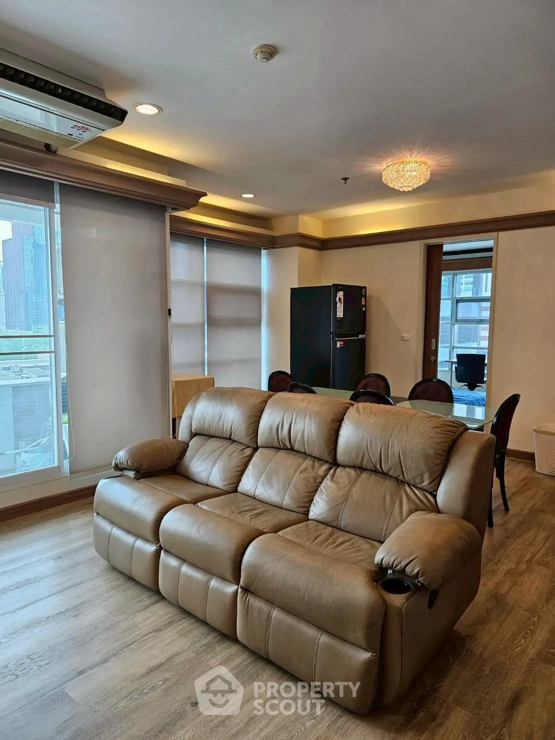 Spacious living room with leather sofa and dining area, featuring large windows and modern lighting.