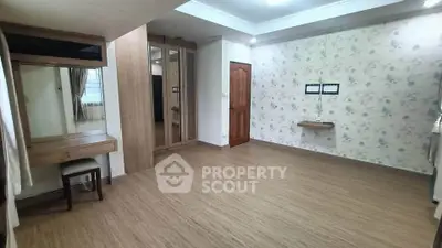 Spacious bedroom with wooden flooring and floral wallpaper, featuring a built-in wardrobe and vanity area.