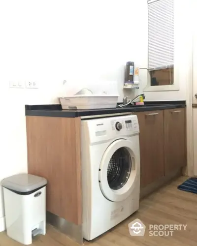 Modern laundry area with washing machine and wooden cabinets in a bright interior.