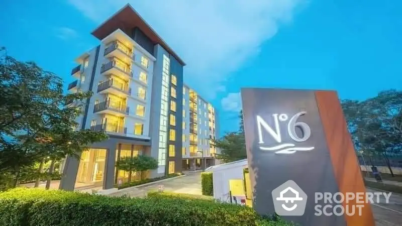 Modern apartment building with illuminated facade and lush greenery at dusk.