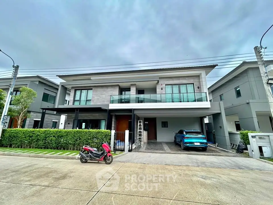 Modern two-story house with balcony, garage, and landscaped front yard in a suburban neighborhood.