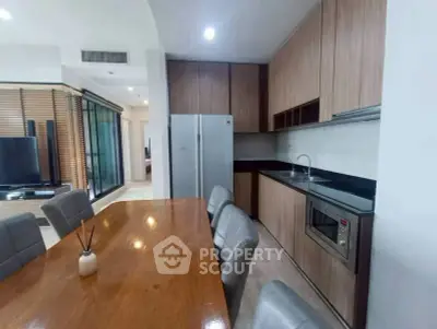 Modern kitchen with sleek wooden cabinets and dining area in open layout.